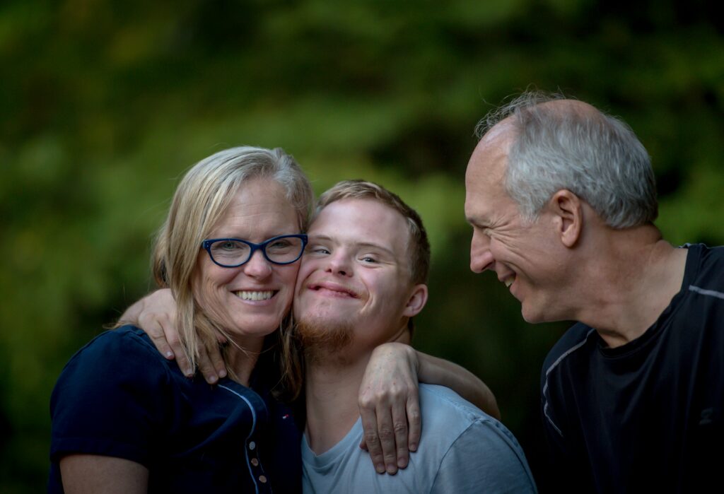 Young man with special needs hugging his mother on the left, father smiling at them both on the right