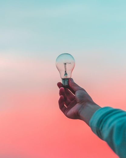 Person holding out lightbulb against a blue and pink backdrop