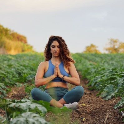 Woman sitting in a field, legs crossed and eyes closed 
