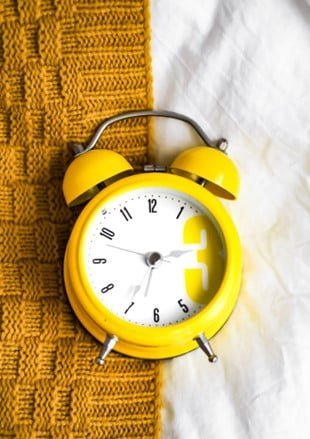 Yellow old-fashioned clock lying on a brown and white blanket.