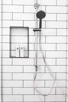 White tile shower with detachable showerhead. Two soap bottles on the side.