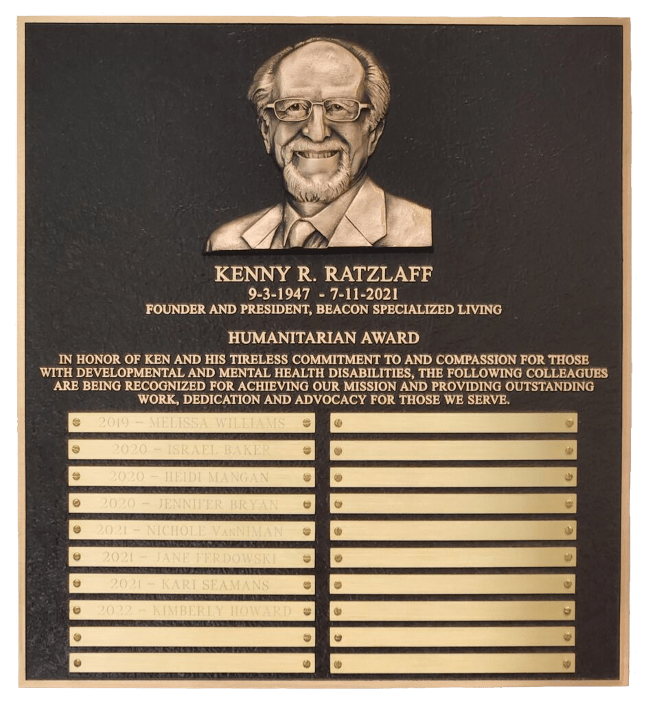 Bronze plaque of the Kenny Ratzlaff Humanitarian Award with his image at the top and name plates of winners on the bottom.