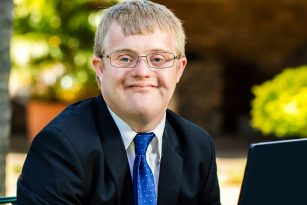 about-us-1 Young man in a suit and tie smiling.