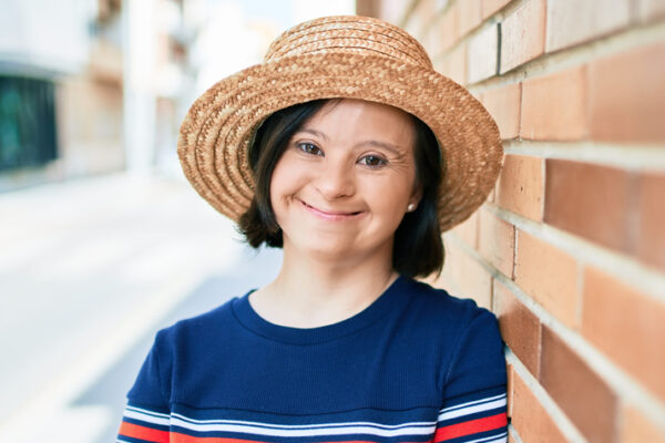 about-us-3 Girls in a sunhat leaning against a brick wall smiling.